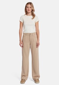 Beige wijde broek met een subtiele textuur, gecombineerd met een aansluitend wit T-shirt met een klein hartlogo op de borst.