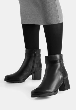 Botines de cuero negro con cierre lateral, acabado pulido, tacón grueso y detalle decorativo de correa alrededor del tobillo.