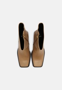 Beżowe skórzane botki za kostkę o gładkim wykończeniu, z kwadratowym noskiem, zapinane na zamek boczny, z czarną gumową podeszwą.