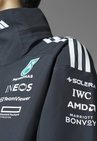 Crna jakna s visokim ovratnikom, koja ima bijele Adidas pruge. Na rukavu se nalaze višestruki logotipi printani u bijeloj boji, uključujući Petronas i IWC.