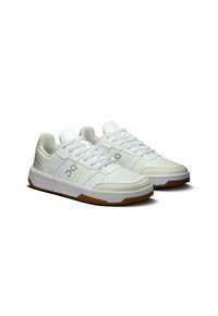 White athletic shoes with a leather upper, perforated toe box, padded collar, and gum rubber outsole. Features flat laces and logo detail.