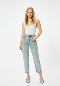 Ljusblå högmidjade jeans med raka ben, fransad fåll och subtila blekningar, kombinerat med en åtsittande vit ribbad tanktop och silverfärgade klackar.