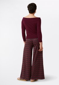 Bordeaux off-shoulder top en wijde broek met een zigzagpatroon in rood en grijs. De broek heeft een hoge taille en is gemaakt van zachte stof.