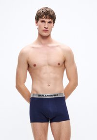 Marineblaue Boxershorts mit einem silbernen elastischen Bund, der "KARL LAGERFELD" in schwarzer Schrift trägt; weicher, dehnbarer Stoff.