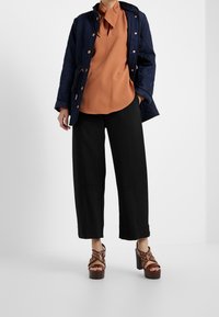Veste matelassée bleu marine, haut couleur rouille avec col à nouer, pantalon large noir et sandales à plateforme marron avec détails ajourés.