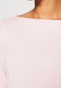 Helles pinkes Oberteil mit weitem Bootsausschnitt, aus weichem Stoff gefertigt. Das Design bietet nahtlose Schultern und eine glatte Textur.
