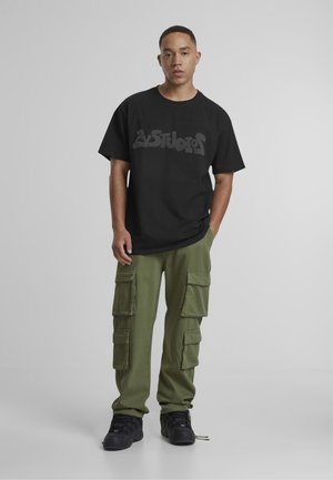 Black t-shirt with large gray graphic, paired with olive green cargo pants featuring multiple pockets, and black sneakers.