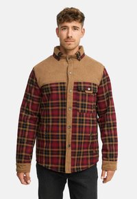 Geruite jas met een rood, zwart en crèmekleurig patroon, corduroy schouderstuk, knoopsluiting aan de voorkant en borstzak.