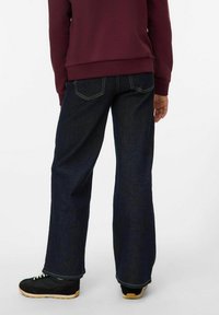 Jean en denim noir avec une coupe droite, taille mi-haute, coutures contrastées et un détail subtil sur la poche arrière. Baskets noires avec une semelle en gomme.