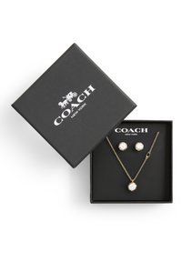 Collana e orecchini oro con cristalli trasparenti tondi incastonati in metallo testurizzato. Presentati in una scatola nera con un logo sul coperchio.
