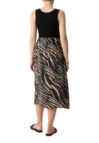 Schwarzes geripptes Tanktop kombiniert mit einem knielangen Rock im Schwarz-Beige-Zebra-Muster, der einen elastischen Bund und flache schwarze Sandalen hat.