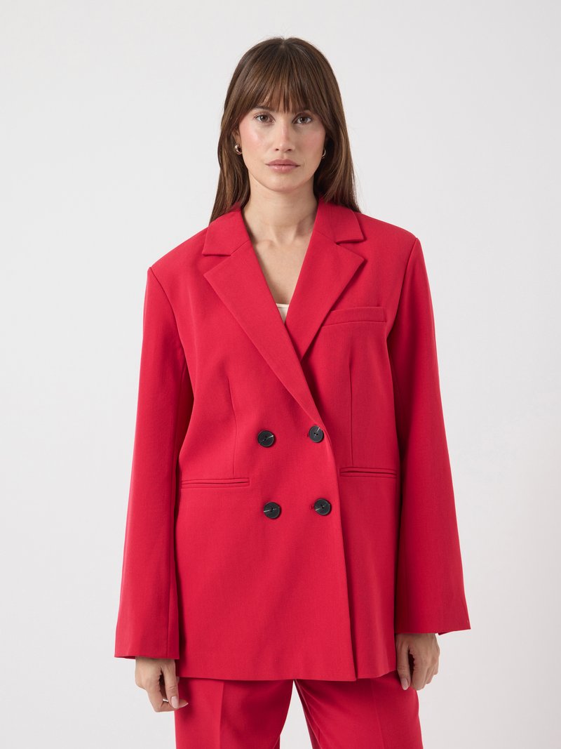 Veste rouge à double boutonnage avec une coupe cintrée, boutons noirs, revers crantés et poches latérales. Tissu lisse et design légèrement oversize.