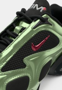 Black sneaker with shiny green synthetic overlays and textured black mesh. Features a red swoosh logo and black accents, with black laces.