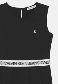 Czarna sukienka z elastycznego materiału, z okrągłym dekoltem, wycięciem na plecach oraz białym paskiem z logo "CALVIN KLEIN JEANS".