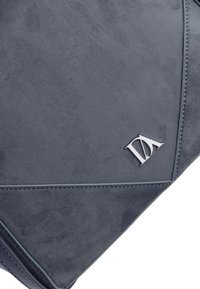 Bolso de ante gris con un diseño geométrico, que presenta costuras en contraste y un acento de logo plateado en la esquina inferior derecha.