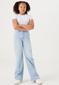 Helle blaue, ausgestellt geschnittene Jeans mit hoher Taille, kombiniert mit einem weißen Kurzarmoberteil mit blauen horizontalen Streifen und gewellten Kanten.