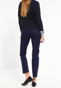 Granatowe spodnie o dopasowanym kroju, wykonane z gładkiego materiału. Projekt charakteryzuje się średnim stanem i wykończeniem z mankietami, uzupełniony czarnymi balerinami.