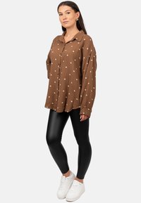 Brown plaid button-up shirt with white heart pattern, long sleeves, paired with black leggings and white sneakers. Smooth texture and casual fit.