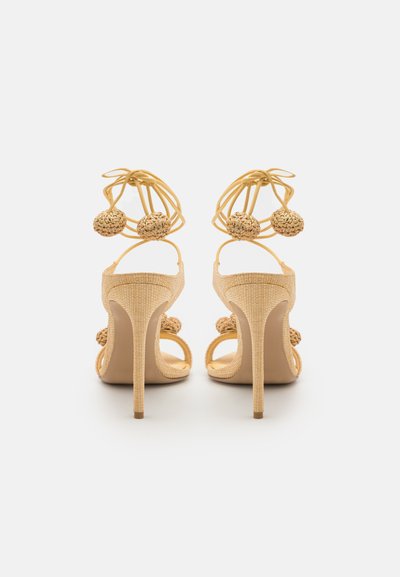 Nude high-heeled sandals with a textured fabric upper, featuring woven ball accents and thin straps, set on a slim stiletto heel.