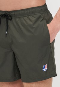 Grønne badebukser laget av lett materiale med elastisk midje, utvendige lommer og K-Way-logo på forsiden.