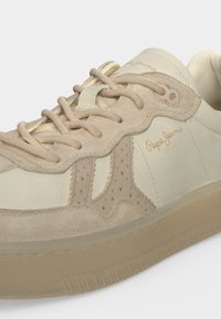 Baskets Pepe Jeans beige et crème avec détails en daim, lacets et semelle en caoutchouc, affichant le logo de la marque sur le côté et sur la languette.