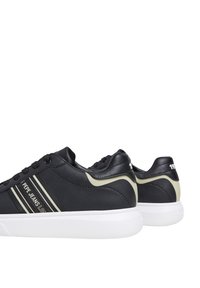 Schwarze Sneakers mit glatter Lederoberfläche, weißer Gummisohle, goldenen Akzenten und gebrandeten Streifen. Die Designs umfassen eine abgerundete Zehenpartie und einen gepolsterten Kragen.