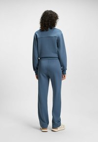Blue athletic tracksuit with a zip jacket and pants. Smooth fabric, relaxed fit, elastic cuffs and waistband. Light stitching detail on the back.