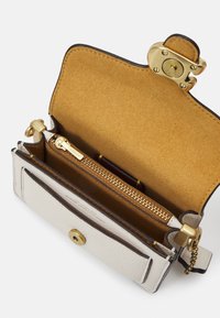 Piccola borsa a tracolla in pelle crema con finitura testurizzata, hardware dorato e interno in suede. Presenta un compartimento con zip e una chiusura a scatto.