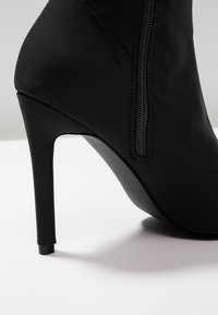 Bota negra de tacón alto con un upper texturizado y suave y un cierre lateral con cremallera. Presenta un tacón de aguja estrecho y una forma contorneada.
