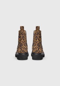 Et par ankelstøvler med leopardmønster og sorte chunky såler vist fra bagsiden på en ensfarvet grå baggrund.