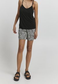 Czarny top bez rękawów w połączeniu z szortami w biało-czarne paski zebry. Model nosi czarne sandały na platformie. Gładki materiał i luźny krój.