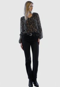 Durchsichtige schwarze Bluse mit Leopardenmuster, geraffte Ärmel; schwarze Jeans mit hohem Bund; schwarze Stiefeletten. Schlichtes, modernes Design.