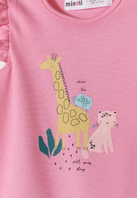 camiseta de algodón rosa con un gráfico de una jirafa amarilla y un leopardo blanco con acentos verdes, mangas con volantes y texto que dice "donde juegan los salvajes".
