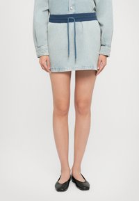 Denim kleita ar gaismu mazgāšanu, ar plašu tumši zilu jostu un atbilstošu auklu, īsa garuma un garām piedurknēm. Melni plakani apavi.