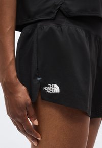 Κοντινό ενός ατόμου που φοράει μαύρα σορτς The North Face με διάτρητες λεπτομέρειες και μικρή πλευρική σχισμή, το χέρι ακουμπά κοντά στο μηρό.