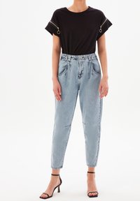 Černé tričko s vyhrnutými rukávy a kapsami na zip v kombinaci se světle modrými džíny s vysokým pasem. Černé sandály na vysokém podpatku se stahovacími pásky.