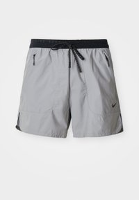 Pantalones cortos de running Nike en gris claro con cintura elástica negra, cordón, bolsillos laterales con cremallera y pequeño logo Swoosh negro en la pierna izquierda.