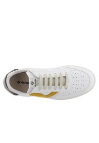 Zapatilla blanca con cordones beiges, detalle lateral amarillo, puntera perforada y refuerzo negro en el talón, vista desde arriba sobre un fondo blanco.