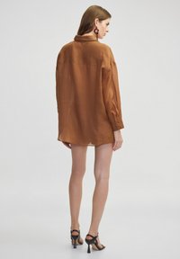 Brown, sheer, button-up shirt with long sleeves, a classic collar, and a relaxed fit, paired with black high-heeled sandals.