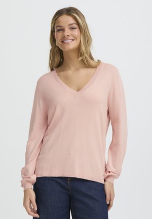 V-Ausschnitt-Pullover mit langen Ärmeln aus weichem rosa Stoff, mit gerippten Bündchen und entspanntem Schnitt, kombiniert mit dunklen Denim-Jeans.