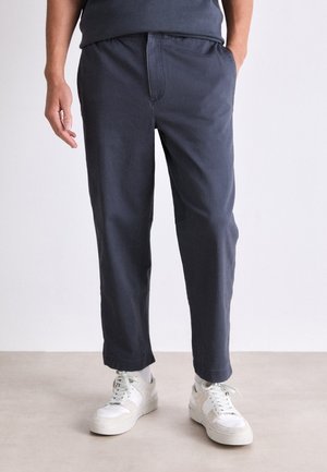 Mørk marinblå bomulls-bukser med elastisk midje, sidelommer og avslappet passform, kombinert med hvite joggesko.
