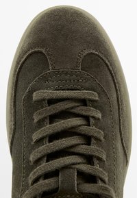 Donkergroene suède sneaker met een afgeronde neus, platte veters en een textuur bovenwerk. Heeft stikaccenten langs de zijkanten.