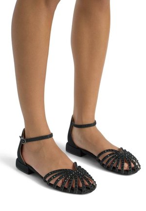 Sandalo nero con design open-toe e motivo a incrocio delle cinghie, arricchito da piccoli borchiette, tacco piatto e cinturino alla caviglia.