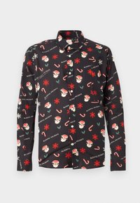 Chemise à manches longues noire avec un imprimé de fête comprenant des visages de Santa, des flocons de neige, des cannes en sucre d'orge et le texte "VACANCES DOUCEURS."