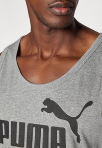 Grå bomulds tanktop med et sort "PUMA" logo og en springende pumagrafik. Bred halsudskæring og blød struktur omkring kraven.