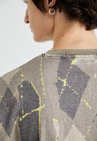Pulover gri cu un model geometric, prezentând forme abstracte în nuanțe de albastru închis și accente strălucitoare de galben, cu guler rotund și material texturat.