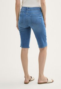 Denim bermuda šortse svijetloplave boje, sa prilagođenim strukom, dva strašnja džepa i porubljenim dizajnom do koljena, uparenim s kremastim sandalama na klizanju.