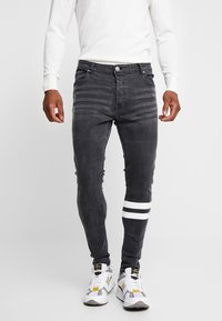 Slim-fit dark gray jeans with a textured finish, featuring white striped accents on one leg and a classic five-pocket design.