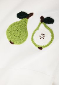 Deux poires crochetées sur tissu blanc, une entière et une tranchée montrant les graines, avec des feuilles vertes et des tiges brunes.