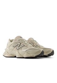 Chaussures de sport beiges avec une tige en daim texturé et en mesh, arborant un logo 'N' bien visible, un talon robuste et une semelle extérieure en caoutchouc noir.